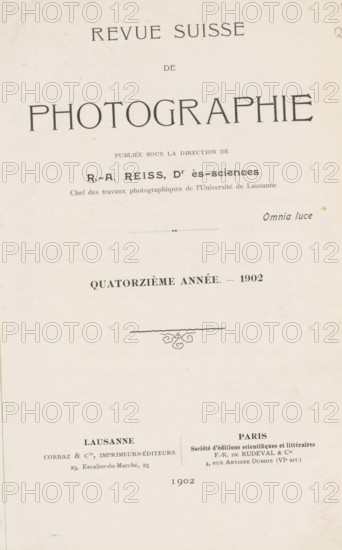 Revue suisse de photographie, book, collector's mark: 'Dr. Frans de vos, 64 tot Rivierenlaan, 64, Deurne, ...', editor (person who revises): Rodolphe Archibald Reiss, 1902, Rodolphe Archibald Reiss, editor (person who revises), textile materials, paper, linen (material), transparent paper, printing, autotype, collotype, height 234 mm x width 172 mm x thickness 34 mm, A vertical page with a pale, slightly textured background showing a large title area at the top and centered ornamental elements and smaller text blocks below; the top contains a wide word in large stylized letters, followed by a narrower word beneath it and a prominent word in very large uppercase letters spanning across the page; below that are several lines of smaller printed text with a small decorative horizontal rule and a small script-style word to the right; further down is a bold centered line of text indicating an annual notation with a year at its end, and beneath it a thin wavy horizontal line with a small flor...