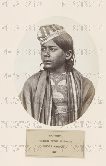 Portrait of an unknown man from the Rajput community originally from Jodhpur in Rajasthan, in Chota Nagpur in eastern India, photograph, page, number: '(25)', inscription: 'RAJPOOT., HINDOO FROM MARWAR., CHOTA NAGPOOR.', photographer: Benjamin Simpson (possibly), Chota Nagpur, c. 1858 - in or before 1868, Jharkhand, paper, albumen print, height 158 mm x width 122 mm, human races, peoples, nationalities, head-gear: cap, A sepia-toned oval portrait shows a young person with dark hair pulled back and wearing a patterned cap tilted slightly forward on the head, looking to the side with a neutral expression; they wear layered garments including a shawl draped over the shoulders and a textured, patterned garment beneath with visible trim along the edges, and the portrait is mounted on a light background with a rectangular label area below.