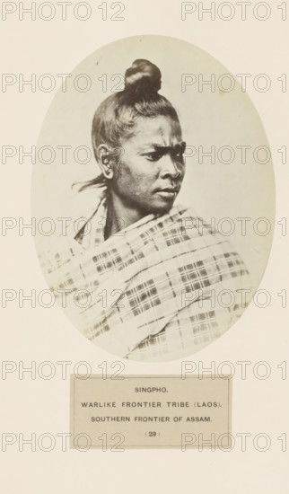 Portrait of an unknown woman from the Singpho tribe of Assam, photograph, page, The tribe is also found in Arunachal Pradesh., number: '(29)', inscription: 'SINGPHO., WARLIKE FRONTIER TRIBE (LAOS)., SOUTHERN FRONTIER OF ASSAM.', photographer: attributed to Benjamin Simpson, Assam, c. 1858 - in or before 1868, Attributed to, paper, albumen print, height 175 mm x width 130 mm, human races, peoples, nationalities, A sepia-toned oval portrait of a person shown from the shoulders up, turned in three-quarter profile to the right, with hair pulled into a top knot and a strand of hair behind the ear, wearing a patterned shawl draped across the shoulders; the portrait is mounted on a pale background with a rectangular label area beneath the oval.