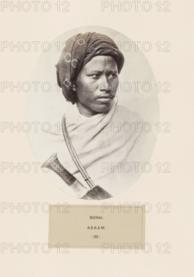 Portrait of an unknown man from the region of Sonai in Assam, photograph, page, number: '(33)', inscription: 'SONAI., ASSAM.', photographer: Benjamin Simpson (possibly), Assam, c. 1858 - in or before 1868, paper, albumen print, height 157 mm x width 120 mm, human races, peoples, nationalities, A sepia-toned oval portrait of a person shown from the shoulders up wearing a patterned headwrap and a draped cloth over the shoulders, the face turned slightly to one side with a neutral expression, visible facial hair and textured skin, and a curved object with a strap crossing the chest partially visible at the lower edge.