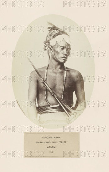 Portrait of an unknown man from the Rengma Naga tribe of Nagaland and Assam, photograph, page, number: '(36)', inscription: 'RENGMA NAGA., MARAUDING HILL TRIBE., ASSAM', photographer: Benjamin Simpson (possibly), Assam, c. 1858 - in or before 1868, paper, albumen print, height 177 mm x width 129 mm, human races, peoples, nationalities, casting weapons: spear, Nagaland, A sepia-toned oval photograph shows a bare-chested man seated and holding a long spear diagonally across his torso, wearing a headpiece with decorative elements and circular adornments at his temples, elongated earrings, and multiple beaded necklaces; a cloth is wrapped around his waist and his gaze is turned to the side.
