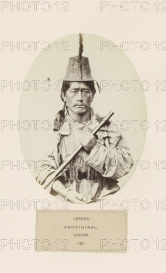 Portrait of an unknown man with a weapon from the Lepcha community of Sikkim, photograph, page, number: '(47)', inscription: 'LEPCHA., ABORIGINAL., SIKHIM.', photographer: Benjamin Simpson (possibly), Sikkim, c. 1858 - in or before 1868, paper, albumen print, height 159 mm x width 120 mm, head-gear: hat, human races, peoples, nationalities, casting weapons, A sepia-toned oval portrait of a person sitting and facing the camera, wearing a tall hat with a vertical ornament extending upward, earrings, and layered clothing with fringed or textured fabric; the person holds a long cylindrical object diagonally across their chest with one hand near the top and the other resting lower, and their expression is neutral.