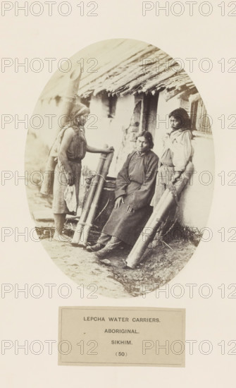 Three water carriers in front of a house from the Lepcha community of Sikkim, photograph, page, number: '(50)', inscription: 'LEPCHA WATER CARRIERS., ABORIGINAL., SIKHIM.', photographer: Benjamin Simpson (possibly), Sikkim, c. 1858 - in or before 1868, paper, albumen print, height 176 mm x width 129 mm, street, human races, peoples, nationalities, An oval sepia photograph shows three people posed in front of a thatched building; one person sits on a low ledge wearing a long dark garment and boots with hands resting on their knees, another stands to the left holding a tall cylindrical bundle and wearing a sleeveless top and a skirt with bare feet, and the third stands to the right leaning against the wall with a wrapped bundle by their side and wearing a long-sleeved shirt and skirt; large cylindrical containers made of a smooth material are propped against the wall and ground, the building has a rough plastered exterior and a sloping thatch roof with visible straw edges, and the ground...