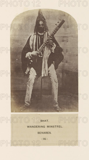 Portrait of an unknown minstrel (Bhat) from Varanasi, Uttar Pradesh, India, photograph, page, inscription, q: 'BHAT., WANDERING MINSTREL., BENARES.', number: '(91)', Varanasi, c. 1858 - in or before 1868, photographer, North India, paper, albumen print, height 134 mm x width 88 mm, minstrel, 'juggler', human races, peoples, nationalities, A monochrome photograph of a seated person wearing a tall conical hat and layered loose clothing, holding a long-necked stringed instrument across their body; the person has a beard and is draped with scarves or cloths, and their hands rest on the instrument’s neck and body. The figure sits against a plain backdrop within an arched frame and wears light-colored trousers and dark footwear. Below the photograph is a rectangular panel containing blocks of printed lines.