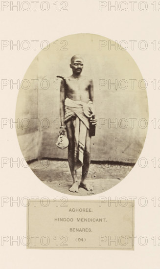Portrait of an unknown man from the Aghori mendicant community of Varanasi, Uttar Pradesh, India, photograph, page, inscription: 'AGHOREE., HINDOO MENDICANT., BENARES.', number: '(94)', Varanasi, c. 1858 - in or before 1868, photographer, North India, paper, albumen print, height 128 mm x width 105 mm, Hinduism, Buddhism, Jainism, human races, peoples, nationalities, A sepia-toned oval photograph of a barefoot man standing against a plain backdrop, his torso bare and a cloth wrapped around his waist and draped over one shoulder, holding a small round object in one hand and a rectangular object in the other, with a neutral facial expression and a shaved head, the image set on a light-colored page with a rectangular bordered area below the oval.