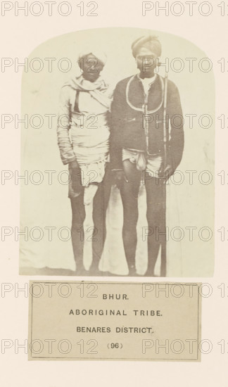 Portrait of two unknown men from the Bhurtiya community of Varanasi district, Uttar Pradesh, India, photograph, page, number: '(96)', inscription: 'BHUR., ABORIGINAL TRIBE., BENARES DISTRICT.', Varanasi, c. 1858 - in or before 1868, photographer, North India, paper, albumen print, height 123 mm x width 96 mm, human races, peoples, nationalities, A faded sepia photograph framed by a rounded top shows two standing men wearing turbans and wrapped cloth garments, both barefoot and facing forward; the man on the right wears a darker jacket-like top with a looped cord over his shoulders and holds a long staff, while the man on the left wears lighter layered wraps around his torso and head and has one arm hanging by his side.