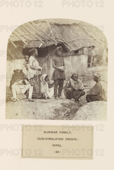 An unknown family on the street in front of houses from the Sunuwar tribe of Nepal, photograph, page, inscription: 'SUNWAR FAMILY., (SUB-HIMALAYAN ORIGIN.), NIPAL.', number: '(60)', Nepal, c. 1858 - in or before 1868, photographer, paper, albumen print, height 120 mm x width 120 mm, family life at home, human races, peoples, nationalities, A sepia-toned photograph shows a group of people gathered outdoors in front of a thatched-roof structure; several adults are seated or crouched on the ground while others stand, wearing layered clothing and shawls, with one standing figure holding a slender staff and another carrying a child on the back; straw and wooden roof supports are visible above them and the ground in front appears uneven with a shallow ditch.
