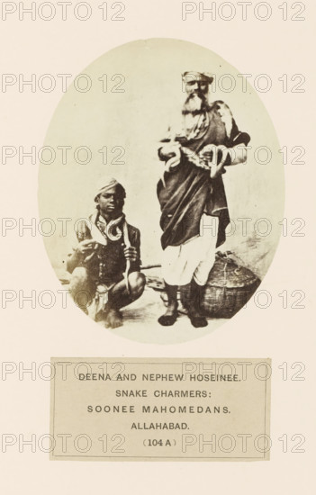 Portrait of Deena and his cousin Hoseinee, two snake charmers from Prayagraj, Uttar Pradesh, India, photograph, page, Prayagraj is also known as Allahabad., inscription: 'DEENA AND NEPHEW HOSEINEE., SNAKE CHARMERS:, SOONEE MAHOMEDANS., ALLAHABAD.', number: '(104 A )', Allahabad, c. 1858 - in or before 1868, photographer, North India, paper, albumen print, height 118 mm x width 95 mm, snakes, human races, peoples, nationalities, An oval sepia photograph shows two men posed against a plain background, one seated on the ground holding a curved object and wearing a headwrap and simple garments, the other standing beside him wearing layered robes, a head covering, and boots, with a long beard and holding a coiled object; a woven basket rests near the standing man's feet.
