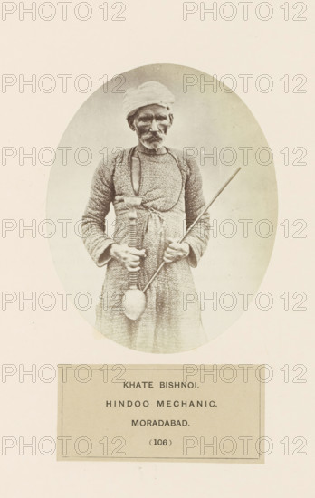 Portrait of Khate with a hookah, a man from the Bishnoi community of Moradabad, Uttar Pradesh, India, photograph, page, inscription: 'KHATE BISHNOI., HINDOO MECHANIC., MORADABAD.', number: '(106)', Moradabad, c. 1858 - in or before 1868, photographer, North India, paper, albumen print, height 120 mm x width 95 mm, water-pipe, hookah, narghile, human races, peoples, nationalities, An oval-framed sepia photograph of an older man standing and facing forward, wearing a wrapped head cloth and a patterned long garment, holding a long thin rod in one hand and a tool with a long handle and rounded end in the other, with a rectangular label area below the oval.