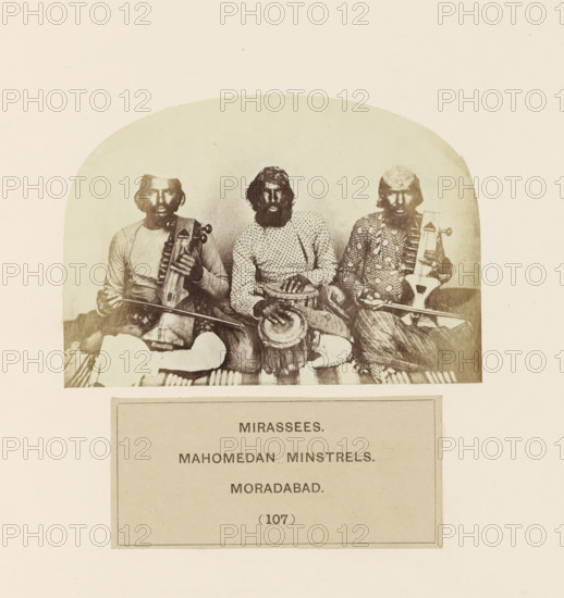 Portrait of three unknown minstrels from Moradabad, Uttar Pradesh, India, photograph, page, inscription: 'MIRASSEES., MAHOMEDAN MINSTRELS., MORADABAD.', number: '(107)', Moradabad, c. 1858 - in or before 1868, photographer, North India, paper, albumen print, height 75 mm x width 107 mm, minstrel, 'juggler', human races, peoples, nationalities, A sepia photograph shows three seated men in traditional clothing, each with a beard and head covering, positioned side by side; the man on the left holds a bowed string instrument across his lap, the man in the center rests his hands on a drum placed between his knees, and the man on the right holds a plucked instrument with a long neck; patterned fabrics and striped textiles are visible beneath them and their garments feature varied prints and textures.