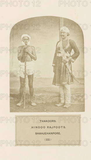 Portrait of two unknown men from the Thakur community of Shahjahanpur, Uttar Pradesh, India, photograph, page, number: '(111)', inscription: 'THAKOORS., HINDOO RAJPOOTS., SHAHJEHANPORE.', Shahjahanpur, c. 1858 - in or before 1868, photographer, North India, paper, albumen print, height 124 mm x width 96 mm, human races, peoples, nationalities, A sepia photograph shows two men standing side by side against a plain background with a curved top border. The man on the left is shirtless and wearing a simple cloth wrapped around his waist and a turban on his head, holding a long staff vertically in front of him with both hands and standing barefoot. The man on the right is dressed in a long ornate coat with patterned trousers and a turban, wearing decorative belts and a sash, with one hand resting on a sheathed curved sword at his side and his feet positioned slightly apart. The ground beneath them appears worn and the image is framed by a light border with a rectangular panel below the phot...