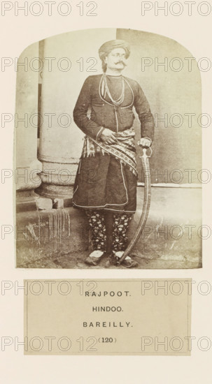 Portrait of an unknown man with a saber from the Rajput community of Bareilly, Uttar Pradesh, India, photograph, page, number: '(120)', inscription: 'RAJPOOT., HINDOO., BAREILLY.', Bareilly, c. 1858 - in or before 1868, photographer, North India, paper, albumen print, height 123 mm x width 96 mm, human races, peoples, nationalities, hacking and thrusting weapons (with NAME), A sepia photograph shows a man standing in front of a plain backdrop and a rounded architectural column; he wears a wrapped turban, a long-sleeved fitted jacket with decorative cords, layered necklaces, and a patterned sash tied at his waist over a knee-length garment; his trousers feature a floral motif and he wears pointed shoes; he holds a curved sword by its hilt with one hand while the other rests near his waist, and his face has a prominent mustache and a neutral expression.