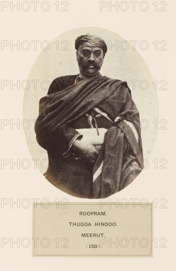 Portrait of Roopram from Meerut, Uttar Pradesh, India, photograph, page, inscription: 'ROOPRAM., THUGGA HINDOO., meerUT', number: '(150)', Meerut, c. 1858 - in or before 1868, photographer, North India, paper, albumen print, height 120 mm x width 95 mm, head-gear: turban, human races, peoples, nationalities, An oval-framed sepia portrait of a man seated and facing forward, wearing a wrapped head covering and a draped garment over one shoulder, with a mustache and neutral expression, his arms folded across his midsection and fabric folds visible around his torso, set against a plain light background and mounted on a light rectangular page.