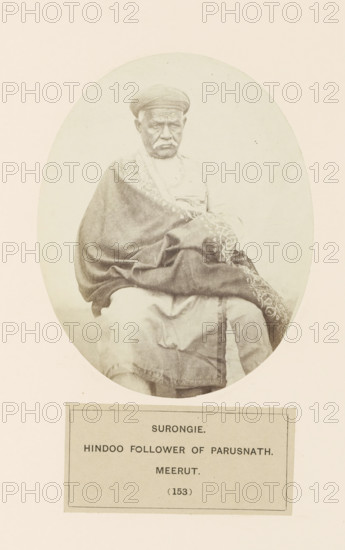 Surongie. Hindoo follower of parusnath. Meerut, Portrait of Shadi Seth, a man from the Jain Bania community (banker) from Bagpat, Uttar Pradesh, India, photograph, page, number: '(153)', inscription: 'SURONGIE., HINDOO FOLLOWER OF PARUSNATH., meerUT.', Bagpat, c. 1858 - in or before 1868, photographer, North India, paper, albumen print, height 129 mm x width 104 mm, head-gear: turban, banker, human races, peoples, nationalities, An oval sepia photograph of an older man seated and facing forward, wearing a rounded cap and a draped patterned shawl over lighter clothing, with his hands resting in his lap and a neutral facial expression; the portrait is mounted on a pale background with a rectangular label area beneath the image.