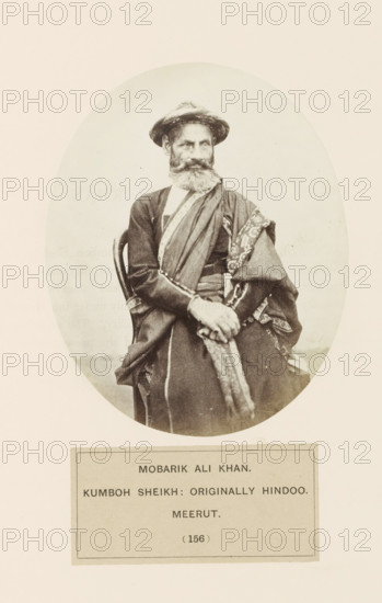 Portrait of Mobarik Ali Khan, a man from the Shaikh community of Meerut, Uttar Pradesh, India, photograph, page, number: '(156)', inscription: 'MOBARIK ALI KHAN., KUMBOH SHEIKH: ORIGINALLY HINDOO., meerUT', Meerut, c. 1858 - in or before 1868, photographer, North India, paper, albumen print, height 129 mm x width 105 mm, head-gear: hat, human races, peoples, nationalities, An oval-framed black-and-white photograph shows an older man seated on a wooden chair, wearing a wide-brimmed hat and a long robe with decorative trim; he has a full beard and mustache and his hands are clasped in his lap, with a patterned sash draped over one shoulder and across his body, and a rectangular label is visible below the oval image.