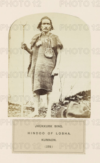 Portrait of Jhukkurk Sing, a man with a walking stick from Kumaon, Uttarakhand, India, photograph, page, inscription: 'JHUKKURK SING., HINDOO OF LOBHA., KUMAON.', number: '(175)', Kumaon, c. 1859 - in or before 1869, photographer, paper, albumen print, height 122 mm x width 96 mm, human races, peoples, nationalities, A sepia-toned photograph of a barefoot man standing on uneven ground, wearing a woven sleeveless garment that reaches to his knees and a small fringed shoulder covering, with a small pouch hanging from a strap across his chest and another pouch at his side; he holds a tall staff with a curved top in one hand, wears a headband, and has shoulder-length hair and a mustache, while a cloth or bundle lies on the ground near his feet and sparse vegetation appears behind him.