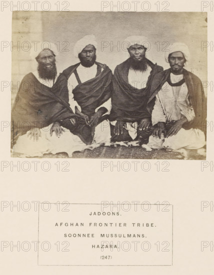 Portrait of four unknown men from the Jadoon tribe of Hazara, Khyber-Pakhtunkhwa, Pakistan, photograph, page, number: '(247)', inscription: 'JADOONS., AFGHAN FRONTIER TRIBE., SOONNEE MUSSULMANS., HAZARA.', Hazara, c. 1862 - in or before 1872, photographer, paper, albumen print, height 86 mm x width 115 mm, human races, peoples, nationalities, A sepia-toned photograph shows four seated men wearing turbans and draped garments, each with visible beards and hands resting on their laps; the men sit closely together on a patterned surface against a plain backdrop, and the image has a faded, aged appearance with light borders around it.