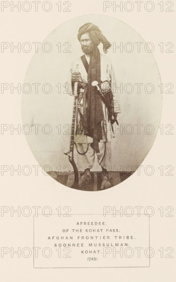 Portrait of an unknown man with a musket from the Afridi tribe of Kohat, Khyber Pakhtunkhwa, Pakistan, photograph, page, inscription: 'AFREEDEE., OF THE KOHAT PASS., AFGHAN FRONTIER TRIBE., SOONNEE MUSSULMAN., KOHAT.', number: '(248)', Kohat, c. 1862 - in or before 1872, photographer, paper, albumen print, height 119 mm x width 95 mm, firearms: rifle, human races, peoples, nationalities, A sepia-toned oval photograph of a barefoot man standing and facing slightly to the side, wearing a wrapped turban and layered loose garments with a long dark scarf draped over his shoulder, holding a long rifle upright with one hand while a sash with attached items crosses his torso, set against a plain light background.