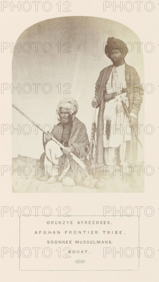 Portrait of two unknown men with muskets from the Afridi tribe of Kohat, Khyber Pakhtunkhwa, Pakistan, photograph, page, inscription, number: '(250)', inscription: 'ORUKZYE AFREEDEES., AFGHAN FRONTIER TRIBE., SOONNEE MUSSULMANS., KOHAT.', Kohat, 1861, photographer, paper, albumen print, height 115 mm x width 87 mm, firearms: rifle, human races, peoples, nationalities, A sepia-toned photograph shows two men in traditional clothing positioned against a plain arched backdrop, one man seated on the ground and the other standing beside him; the seated man wears a wrapped head covering and layered garments with draped fabric and holds a long rifle across his lap, while the standing man wears a turbanlike headwrap, a long outer robe over lighter inner garments, and holds a long firearm upright by his side and a shorter object at his waist; both men have facial hair and barefoot feet are visible, with the base area showing a textured surface and some bundled items near the seated man's feet.