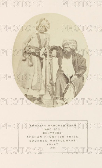 Portrait of Khwajah Mahomed Khan and his son from the Khattak tribe of Kohat, Khyber Pakhtunkhwa, Pakistan, photograph, page, number: '(251)', inscription: 'KHWAJAH MAHOMED KHAN, AND SON., KHUTTUKS., AFGHAN FRONTIER TRIBE., SOONNEE MUSSULMANS., KOHAT.', Kohat, c. 1862 - in or before 1872, photographer, paper, albumen print, height 107 mm x width 87 mm, firearms: rifle, human races, peoples, nationalities, An oval sepia photograph shows two men in traditional clothing against a plain background; the man on the left stands with a turban wrapped around his head, wearing a long garment with a sash and a belt from which small pouches hang, one hand resting on a tall vertical object and the other on his hip, while the man on the right sits with a turban and a full beard, wearing layered robes and holding a curved object across his lap, his elbow resting on the same vertical object between them.