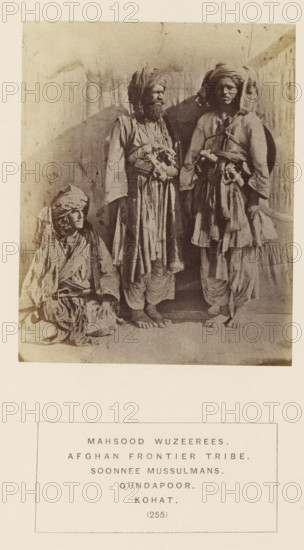 Portrait of three unknown men from the Mahsud tribe of Kohat, Khyber Pakhtunkhwa, Pakistan, photograph, page, inscription: 'MAHSOOD WUZEEREES., AFGHAN FRONTIER TRIBE., SOONNEE MUSSULMANS., GUNDAPOOR., KOHAT.', number: '(255)', Kohat, c. 1862 - in or before 1872, photographer, paper, albumen print, height 111 mm x width 90 mm, head-gear: turban, human races, peoples, nationalities, The sepia photograph shows three individuals wearing layered, loose garments and turbans, with one person seated on the ground to the left and two standing in the center and right; the seated figure has a wrapped head covering and draped cloth around the shoulders, the central standing figure has a full beard, a long outer robe with decorative elements at the waist and layered lower garments, and bare feet visible on the floor, while the right standing figure wears a turban, a belted tunic with hanging fabric and layered lower garments and also has bare feet; a plain backdrop with faint vertical marks and a s...