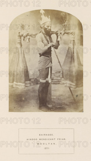 Portrait of a mendicant (Bairagi) from Multan, Punjab, Pakistan, who carries water from the Ganga river, photograph, page, number: '(277)', inscription: 'BAIRAGEE., HINDOO MENDICANT FRIAR., MOOLTAN.', Multan, c. 1862 - in or before 1872, photographer, paper, albumen print, height 145 mm x width 105 mm, religious functions, Hinduism, Buddhism, Jainism, human races, peoples, nationalities, A sepia-toned photograph shows a standing man wearing a tall pointed headpiece and layered necklaces, with a wrapped garment around his waist and bands around his thighs; he holds a long staff with one hand and supports a horizontal pole across his shoulders from which hang two tall conical cloth bundles decorated at the bases and small hanging bells, with tassels or bundles attached near the top of the pole, and the scene is framed within an arched border on a pale background.