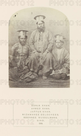 Portrait of Danja Khan, Ahmed Khan and Jaffur Khan, Sindh, Pakistan, photograph, page, Left: Ahmed Kan, center: Danja Khan, right: Jaffur Khan., number: '288.', inscription: 'DANJA KHAN., AHMED KHAN., JAFFUR KHAN., NIZAMANEE BELOCHEES., SOONNEE MUSSULMANS., SIND.', photographer: Henry Charles Baskerville Tanner (possibly), c. 1862 - in or before 1872, paper, albumen print, height 115 mm x width 88 mm, head-gear: hat, ruler, sovereign, human races, peoples, nationalities, A faded sepia photograph shows three seated men wearing tall cylindrical hats with flat tops; the central figure is larger and positioned slightly higher than the other two, with a full beard and hands resting on his knees, wearing layered loose garments and sandals. The man on the left wears a patterned jacket with decorative elements and sits with his hands on his thighs, a folded striped textile at his feet. The man on the right wears a striped outer garment over a lighter inner piece and sits with his hands clasped...
