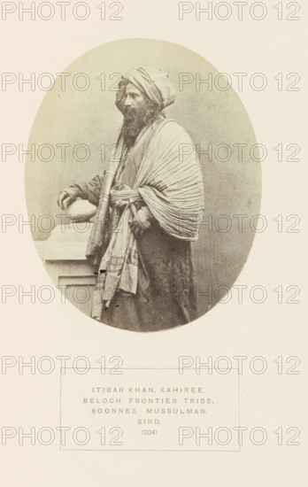 Portrait of Itibar Khan, a chief of the Kahiri Baloch tribe in Sindh, Pakistan, photograph, page, inscription: 'ITIBAR KHAR, KAHIREE., BELOCH FRONTIER TRIBE., SOONNEE MUSSULMAN., SIND.', number: '(304)', photographer: Henry Charles Baskerville Tanner (possibly), Sindh, photographer: William Robert Houghton (possibly), c. 1862 - in or before 1872, paper, albumen print, height 128 mm x width 103 mm, ruler, sovereign, head-gear: turban, human races, peoples, nationalities, A sepia-toned oval portrait shows a bearded man in traditional layered garments and a wrapped turban, standing in profile with one hand resting on a stone ledge and the other holding a rolled cloth or staff, his outer draped shawl displaying pronounced folds and pleats and his clothing featuring textured patterns.