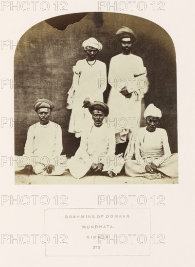 Portrait of five unknown priests (brahmins) from Mandhata, Madhya Pradesh, India, photograph, page, Oomkar from the original title refers to the Omkareshwar Temple located in Mandhata., inscription: 'BRAHMINS OF OOMKAR., MUNDHATA., NIMAUR.', number: '373.', photographer: James John Waterhouse (possibly), Mandhata, 1862, Central India, paper, albumen print, height 125 mm x width 119 mm, head-gear: turban, religious functionaries, Hinduism, Buddhism, Jainism, human races, peoples, nationalities, A sepia-toned photograph framed by an arched background shows five seated and standing men wearing light-colored traditional garments and turbans; two men stand behind three men who sit cross-legged on the ground, all facing forward with neutral expressions, hands resting in laps or clasped, and a plain dark backdrop behind them with a lighter border surrounding the image.