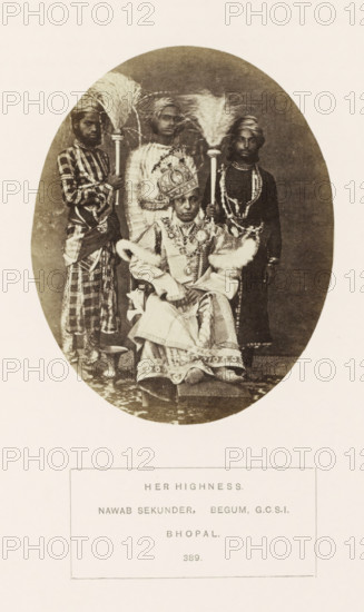 Portrat of Sekunder Begum, a queen of Bhopal, Madhya Pradesh, India, photograph, page, inscription: 'HER HIGHNESS., NAWAB SEKUNDER, BEGUM GCSI, BHOPAL.', number: '389.', photographer: James John Waterhouse (possibly), Bhopal, 1862-11, Central India, paper, albumen print, height 119 mm x width 95 mm, ruler, sovereign - BB - female ruler, human races, peoples, nationalities, An oval sepia photograph shows a seated woman wearing an ornate headdress and richly patterned robes with fur trim, seated on a low platform with her hands resting in her lap; behind her stand three attendants dressed in varied traditional clothing and turbans, two of whom hold long handled ceremonial fans with large feathered plumes, while the third wears layered necklaces and beads; the background is plain and dark, and the image sits on a lighter rectangular page with a bordered area below containing printed lines of text that are not described.
