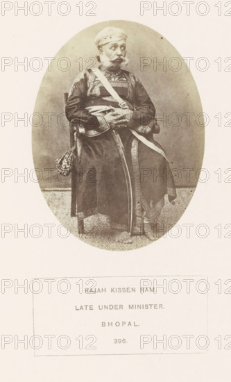 Portrait of Rajah Kissen Ram, a minister from Bhopal, Madhya Pradesh, India, photograph, page, number: '396.', inscription, q: 'RAJAH KISSEN RAM., LATE UNDER MINISTER., BHOPAL.', photographer: James John Waterhouse (possibly), Bhopal, 1862, Central India, paper, albumen print, height 102 mm x width 78 mm, human races, peoples, nationalities, ministerial council, An oval sepia photograph shows an older man seated on a wooden chair wearing a turban and a long embroidered robe with patterned trim; a sash crosses his chest and another hangs by his side, and he has a mustache and beard with hands folded over his lap; the floor beneath him has a patterned rug and his bare feet are visible.