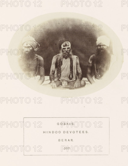 Portrait of three unknown men from the Gosain community of the former Berar in central India, photograph, page, inscription: 'GOSAIS., HINDOO DEVOTEES., BERAR.', number: '397.', photographer: James Mulheran (possibly), Berar, 1862, paper, albumen print, height 77 mm x width 104 mm, human races, peoples, nationalities, A faded oval photograph shows three seated men with bare torsos and long beards arranged side by side against a dark background, each wearing headwraps and multiple bead necklaces, the center figure with painted markings on his face and arms and draped cloth across his shoulder, the left and right figures turned slightly inward with similar beads and cloth wraps, the image surrounded by a pale border and positioned above a rectangular boxed area containing printed lines of text.