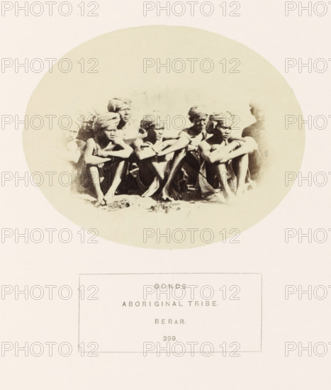Group portrait of people from the Gond tribe of the former Berar in central India, photograph, page, number: '399.', inscription: 'GONDS., ABORIGINAL TRIBE., BERAR.', photographer: James Mulheran (possibly), Berar, 1862, paper, albumen print, height 95 mm x width 120 mm, human races, peoples, nationalities, A faded oval photograph shows a group of people sitting closely together with arms resting on their knees; they wear headwraps and simple clothing, their skin tones rendered in sepia, and the image has a soft, high-contrast look with faces and limbs partially obscured by light areas and shadow.