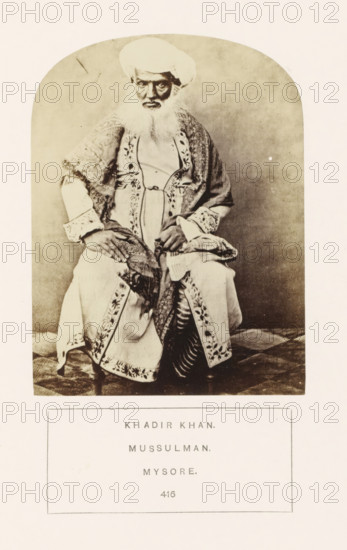 Portrait of Khadir Khan of Mysore, Karnataka, India, photograph, page, inscription: 'KHADIR KHAN., MUSSULMAN., MYSORE.', number: '416.', Mysore, c. 1865 - in or before 1875, photographer, South India, paper, albumen print, height 115 mm x width 87 mm, head-gear: turban, human races, peoples, nationalities, A seated elderly man wearing a turban and a long embroidered robe with patterned borders looks toward the camera, his hands resting on his lap and a shawl draped over one shoulder, the photograph framed within a rounded-arch matte and set above a blank rectangular area.