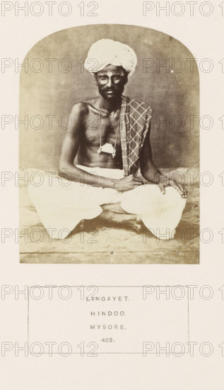 Portrait of an unknown man from the Lingayat community of Mysore, Karnataka, India, photograph, page, inscription: 'LINGAYET., HINDOO., MYSORE.', number: '422.', Mysore, c. 1865 - in or before 1875, photographer, South India, paper, albumen print, height 115 mm x width 87 mm, human races, peoples, nationalities, A sepia-toned photograph shows a seated man wearing a wrapped turban and loose white lower garment, posed with one leg crossed and one hand resting on his knee; he is bare-chested with a long necklace holding a small rectangular object, and a patterned cloth draped over one shoulder, set against a plain backdrop with a light border around the image.