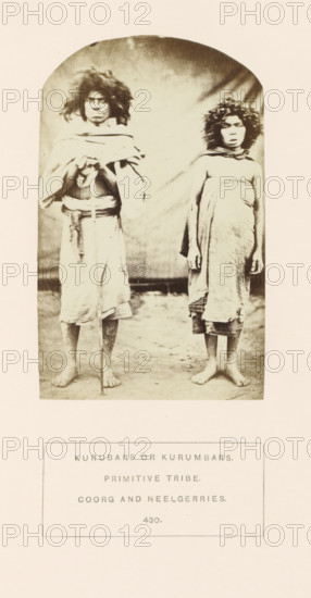 Portrait of Madeo and Kali, siblings from the Kurumba tribe of the Nilgiri mountains in Tamil Nadu, India, photograph, page, inscription: 'KURUBARS OR KURUMBARS., PRIMITIVE TRIBE., COORG AND NEELGERRIES', number: '430.', Nilgiris, c. 1865 - in or before 1875, photographer, South India, Tamil Nadu, paper, albumen print, height 130 mm x width 81 mm, brothers or sisters (second degree family relationships), human races, peoples, nationalities, A sepia-toned photograph shows two barefoot young people standing side by side on a plain ground in front of a backdrop with a soft gradient. Both have thick, curly hair and neutral facial expressions. The person on the left wears a wrapped garment over the shoulders and around the waist, holds a vertical staff with both hands, and has a visible belt or cord at the waist. The person on the right is wrapped in a single cloth draped around the torso and hanging down, with arms relaxed at the sides. The image is framed with rounded top corners and is m...