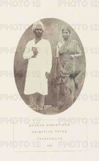 Portrait of an unknown man and woman from the Nadar community of Travancore, India, photograph, page, Travancore was a historic country in the southern tip of India. The Nadar community is also known as Shanar., inscription: 'SHAHAR CHRISTIANS., PRIMITIVE TRIBE., TRAVANCORE.', number: '453.', Travancore, c. 1865 - in or before 1875, photographer, paper, albumen print, height 103 mm x width 77 mm, human races, peoples, nationalities, An oval sepia photograph shows a man and a woman standing side by side against a plain backdrop; the man on the left wears a light long tunic and a wrapped head covering while holding a book against his chest, and the woman on the right wears a draped sari with one arm bent and her hand resting near her waist; both faces are visible and their clothing textures and folds are noticeable.