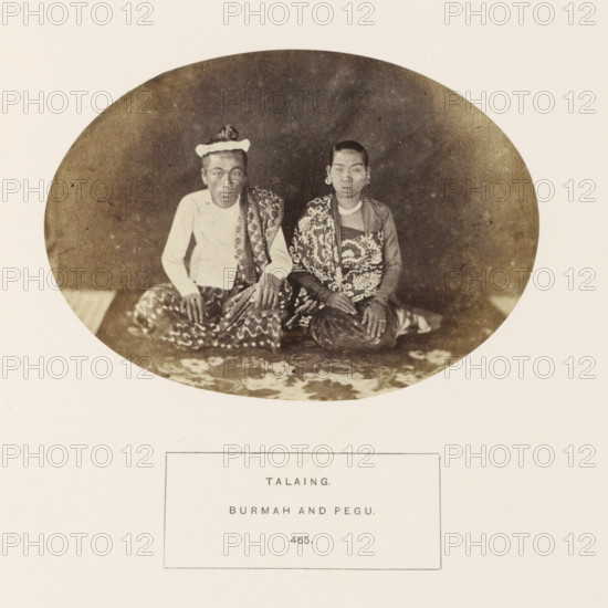 Portrait of a man and woman from the Mon tribe of Myanmar, photograph, page, number: '465.', inscription: 'TALAING., BURMAN AND PEGU.', Myanmar, c. 1865 - in or before 1875, photographer, paper, albumen print, height 98 mm x width 138 mm, human races, peoples, nationalities, An oval sepia photograph shows two seated individuals on a patterned floor covering against a dark backdrop; the person on the left wears a light-colored long-sleeved top, a patterned sarong, and a headwrap, with hands resting on their knees, while the person on the right has short hair, large circular ear ornaments, a patterned garment draped over one shoulder, and hands resting together on their lap.