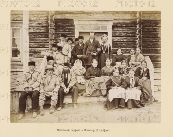 Matrimonio lappone a Bossekop (Altenfjord), Group portrait at a Saami wedding in Bossekop, photograph, page, number: 'Tavola XXXII.', photographer: Paolo Mantegazza, Bossekop, photographer: Carlo Pietro Stefano Sommier, c. 1870 - in or before 1880, paper, albumen print, height 156 mm x width 210 mm, Photo in photo section at the back., civil marriage ceremony, bride and groom in wedding-dress, anonymous historical persons depicted in a group, in a group-portrait, A sepia-toned photograph showing a group of people arranged on and in front of wooden steps leading to a log building with visible horizontal logs and carved corner notches, a doorway with a simple framed transom, and a window with lace curtains; the group includes men and women wearing a variety of clothing such as coats, shawls, headscarves, fur hats, and traditional-looking garments, with some individuals seated on the steps and others standing behind them, one couple standing at the doorway with the woman wearing a floral ...