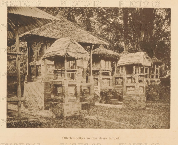 View of sacrificial temples, Sacrificial temples in the Dessa temple, page, photomechanical print, maker: Christiaan Johan Neeb, c. 1892 - in or before 1897, paper, collotype, photoprint, height 124 mm x width 166 mm, trees, places and objects of worship, non-Christian religions, Indonesia, A sepia-toned photograph showing a row of small raised structures with thatched roofs set on carved stone or brick bases, each structure supported by wooden posts and partially enclosed by low ornate balustrades, with larger thatched and corrugated roofs visible behind them, dense foliage of tall trees in the background, and a ground area with grass and scattered stonework in the foreground.