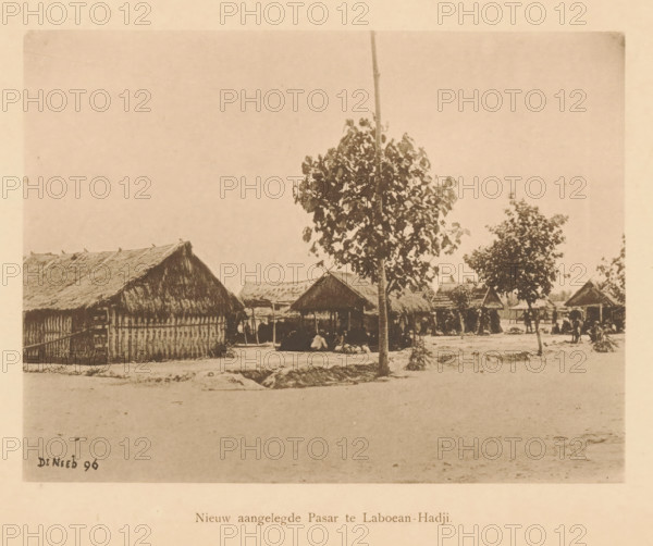 Newly constructed Pasar at Laboean-Hadji, View of a market, page, photomechanical print, maker: Christiaan Johan Neeb, c. 1892 - in or before 1897, paper, collotype, photoprint, height 123 mm x width 168 mm, market, Indonesia, A sepia-toned photograph shows a dirt foreground leading to a row of thatched-roof huts and open-sided shelters with woven walls and raised roofs, a tall tree with a slender trunk and a leafy canopy standing near the center, additional smaller trees scattered among the huts, a few people seated or gathered beneath the shelters, simple fencing and posts around some structures, and a mostly clear sky above.