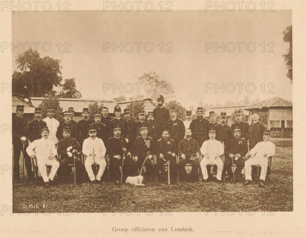 Group portrait of officers of Lombok, Group of officers of Lombok, page, photomechanical print, maker: Christiaan Johan Neeb, c. 1892 - in or before 1897, paper, collotype, photoprint, height 119 mm x width 165 mm, anonymous historical persons depicted in a group, in a group-portrait, ranks (in the army, navy, air force), A sepia-toned group portrait of uniformed men arranged in rows outdoors, with seated figures in front and standing figures behind, many wearing dark military-style coats and peaked caps while a few wear lighter uniforms; a small dog lies on the ground in front of the seated row; trees and simple buildings with thatched or sloped roofs are visible in the background under a wide sky.