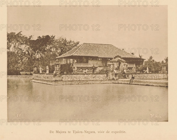View of a temple on the bank of a river, Majora at Tjakra-Negara, before the expedition, page, photomechanical print, maker: Christiaan Johan Neeb, c. 1892 - in or before 1897, paper, collotype, photoprint, height 121 mm x width 166 mm, river bank, temple, shrine, non-Christian religions, Indonesia, A sepia-toned photograph showing a low building with a tiled roof set on a raised stone platform surrounded by water, ornamental stone railings and carved gate structures in front, trees and foliage behind the building, small human figures positioned along the platform near the gate and edges, and a person seated at the platform edge with legs hanging toward the water.