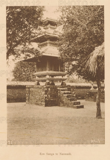 A Sanga at Narmade, A temple at Narmada, page, photomechanical print, maker: Christiaan Johan Neeb, c. 1892 - in or before 1897, paper, collotype, photoprint, height 168 mm x width 118 mm, landscapes, temple, shrine, non-Christian religions, Lombok, Narmada, A sepia-toned photograph showing a multi-tiered pagoda-like structure with ornate layered roofs partially obscured by large leafy trees; the building sits on a raised brick platform with a short flight of stone steps leading up to it and decorative stone supports along the platform edge; a tree trunk with a cluster of long, thin palm-like leaves is visible on the right foreground and a low brick wall extends behind the platform; the ground in front of the structure is open and bare.