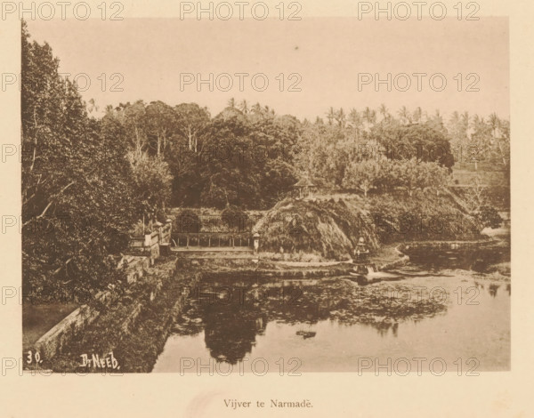 View of a water at Narmada, Pond at Narmade, page, photomechanical print, maker: Christiaan Johan Neeb, c. 1892 - in or before 1897, paper, collotype, photoprint, height 121 mm x width 167 mm, landscapes with waters, waterscapes, seascapes (in the temperate zone), Lombok, Narmada, A sepia-toned photograph shows a landscape with dense trees and tall palms along the upper portion, a thatched mound and a small pavilion near the center, a stone wall and a bridge-like structure extending across a water body, and a calm reflective pond in the foreground bordered by vegetation.