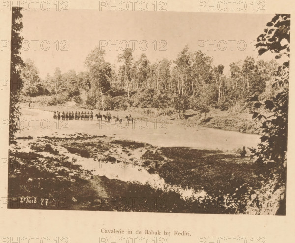 View of the cavalry in a river near Kediri, Cavalry in the Babak near Kediri, page, photomechanical print, maker: Christiaan Johan Neeb, c. 1892 - in or before 1897, paper, collotype, photoprint, height 120 mm x width 167 mm, trees, river, land forces (cavalry, horsemen), Indonesia, A sepia-toned landscape photograph showing a wide shallow river with a line of mounted figures crossing from one bank to the other, leafy trees and dense forest rising behind the far bank, rocky and uneven riverbed in the foreground, dark silhouetted foliage framing the left and right edges of the image, and a small figure seated near the near bank on the right.