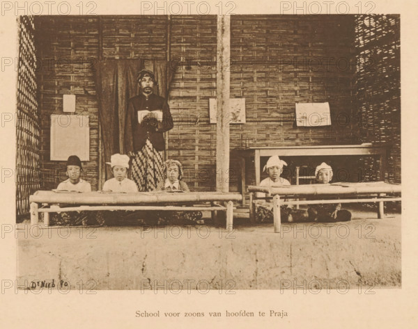 School for sons of headmasters in Praja, View of unknown children and an unknown man in a school, page, photomechanical print, maker: Christiaan Johan Neeb, c. 1892 - in or before 1897, paper, collotype, photogravure, height 118 mm x width 162 mm, historical persons, boy (child between toddler and youth), adult man, Indonesia, A sepia photograph showing a woven bamboo wall with a vertical post near the center and curtains hanging behind a standing man who holds an open book, wearing a dark jacket and patterned lower garment, with five seated boys arranged on low wooden benches in front of him wearing light shirts and various head coverings, some with fabric wraps, and small books or papers on the benches, with a simple wooden railing in front and framed rectangular objects hung on the wall.