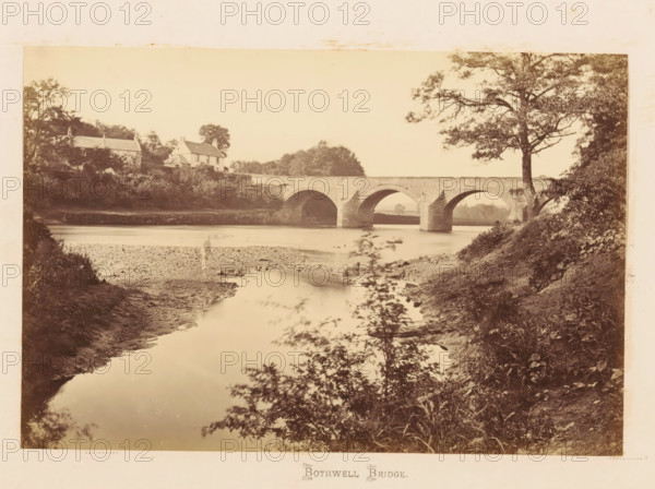 View of Bothwell Bridge over the Clyde, Bothwell Bridge, photograph, page, South Lanarkshire, c. 1862 - in or before 1867, photographer, paper, albumen print, height 120 mm x width 179 mm, river, landscapes with waters, waterscapes, seascapes (in the temperate zone), bridge, A sepia-toned riverscape shows a stone arched bridge spanning calm water, with three large rounded arches visible and masonry piers extending into the river. On the far bank left of the bridge there are houses partially hidden by trees and shrubs, one with a pitched roof and chimneys. Vegetation lines both riverbanks, including bushes and grasses on the near bank and taller trees framing the right side of the image, where a large tree with spreading branches stands near the bridge. The river surface reflects the bridge and surrounding foliage, and a muddy, pebbled shoreline is visible beneath the nearest bank. The sky above is light and unobstructed.