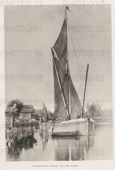 A Norwich barge, on the yare, Barge with two men, page, photomechanical print, photographer: John Payne Jennings, Norfolk Broads, cliché maker: Permanent Photo Printing Works, Ashtead, Surrey, c. 1886 - in or before 1891, paper, collotype, photoprint, height 167 mm x width 115 mm, Print opposite title page., sailing-ship, sailing-boat, river, landscapes with waters, waterscapes, seascapes (in the temperate zone), A tall sailboat with its sails partially unfurled is moored on calm water, its masts and rigging rising high into the sky with a small flag at the top. The boat's hull sits low in the water and a smaller rowboat is tied alongside it. Reflections of the masts and hull appear on the smooth surface of the water. Along the shoreline there is a cluster of buildings with pitched roofs, a tree with textured foliage, and patches of reeds and grass at the water's edge. The image is rendered in a monochrome tone with a soft, evenly lit sky occupying much of the background.