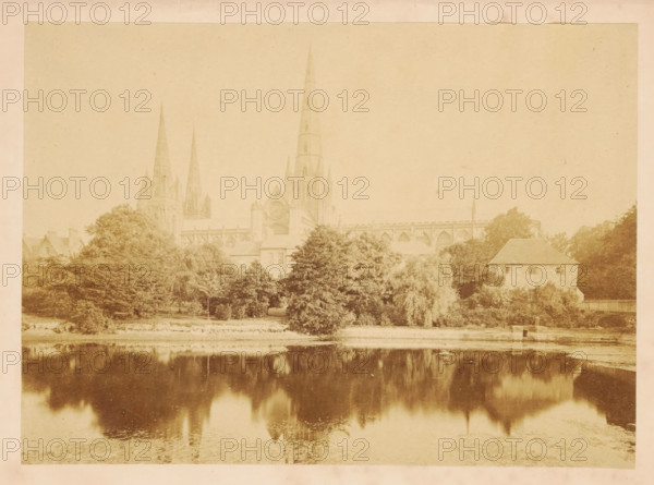 A history of Lichfield Cathedral, from its foundation to the present time : with a description of its architecture and monuments, book, annotation: '1970, 5 photographs, by JB Stone - late Sir Benjamin Stone, £40', annotation: 'late Sr Benjain Stone MP + photographer', annotation: 'Oct 1995', bookplate: 'Post tenebras lucem, e-libris, Hugh Br...', retailer's mark: 'Galloway & Porter (Charles P. Porter), New & second-hand bookseller, 30, Sidney street, Cambridge', writer (clerical worker): John Benjamin Stone, publisher: Longmans, Green, Reader, & Dyer, London, 1870, John Benjamin Stone, Longmans, writer (clerical worker), publisher, textile materials, paper, linen (material), printing, wood engraving, albumen print, color on cut, height 217 mm x width 172 mm x thickness 24 mm, A sepia-toned photograph showing a large Gothic cathedral with tall pointed spires rising behind a row of trees, bushes, and buildings along a riverbank, with the cathedral and surrounding vegetation reflected in...